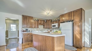Une cuisine avec des meubles de rangement en bois, un îlot central, un four à micro-ondes et un réfrigérateur.