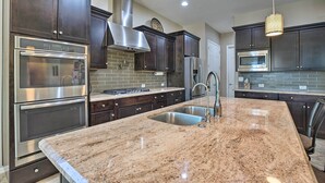 A modern kitchen with dark wood cabinets, stainless steel appliances, a granite countertop, and recessed lighting. - Modern Azure Home w/ Beautiful Patio, Pool & Spa! (Goodyear)