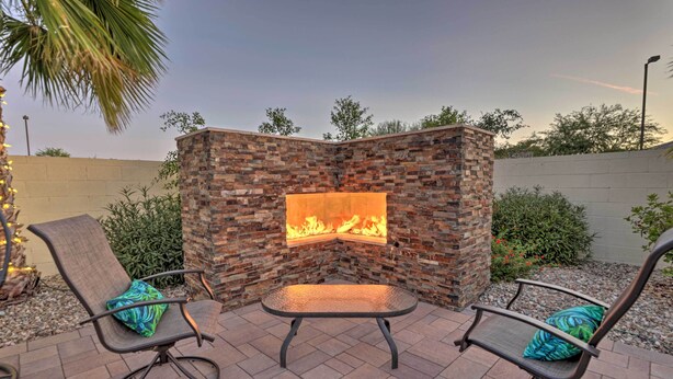 An outdoor seating area with a stone wall and a fire feature. - Modern Azure Home w/ Beautiful Patio, Pool & Spa! (Goodyear)