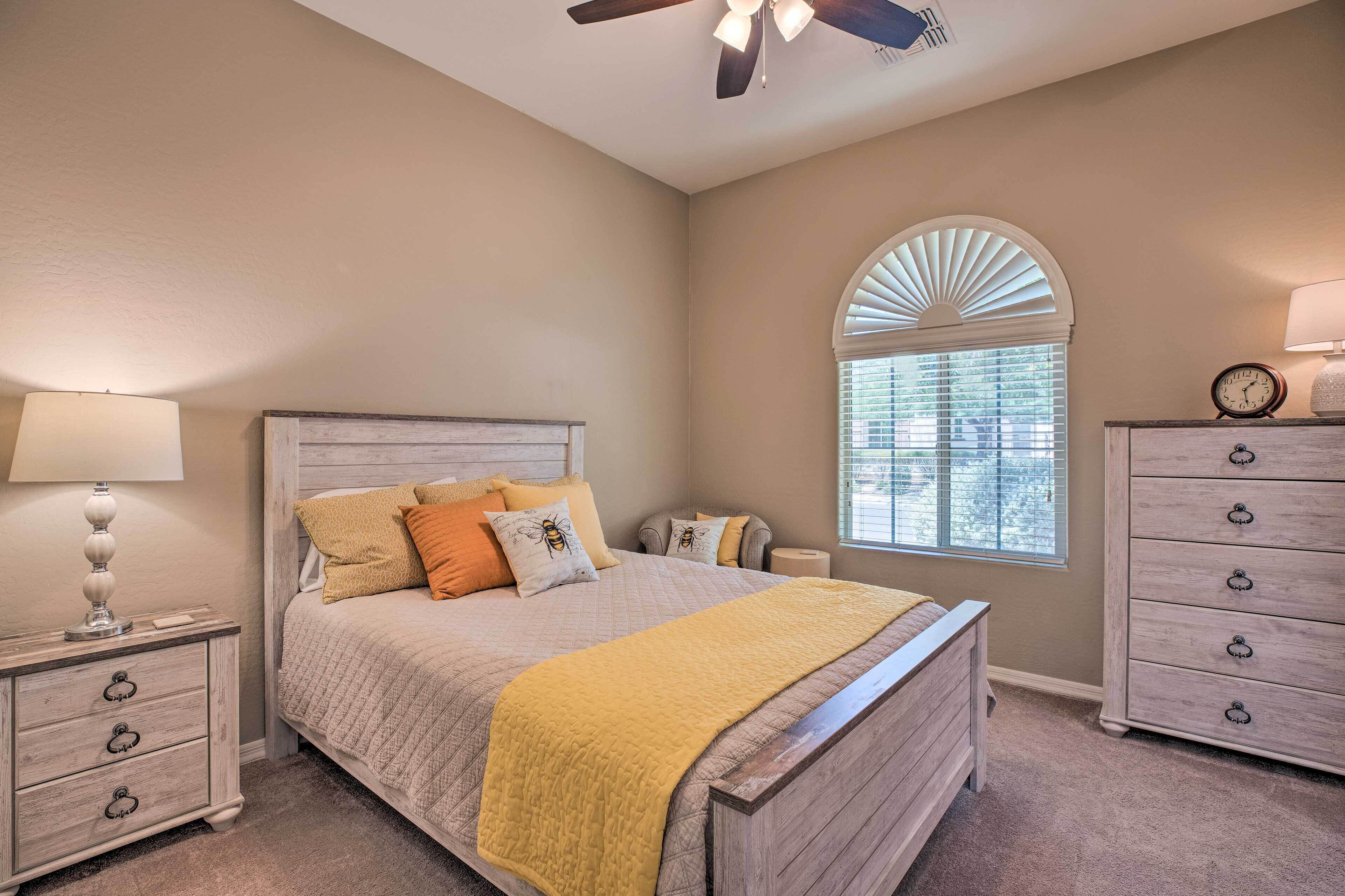 A bedroom with a bed, a nightstand, a dresser, a ceiling fan, and a window with blinds.