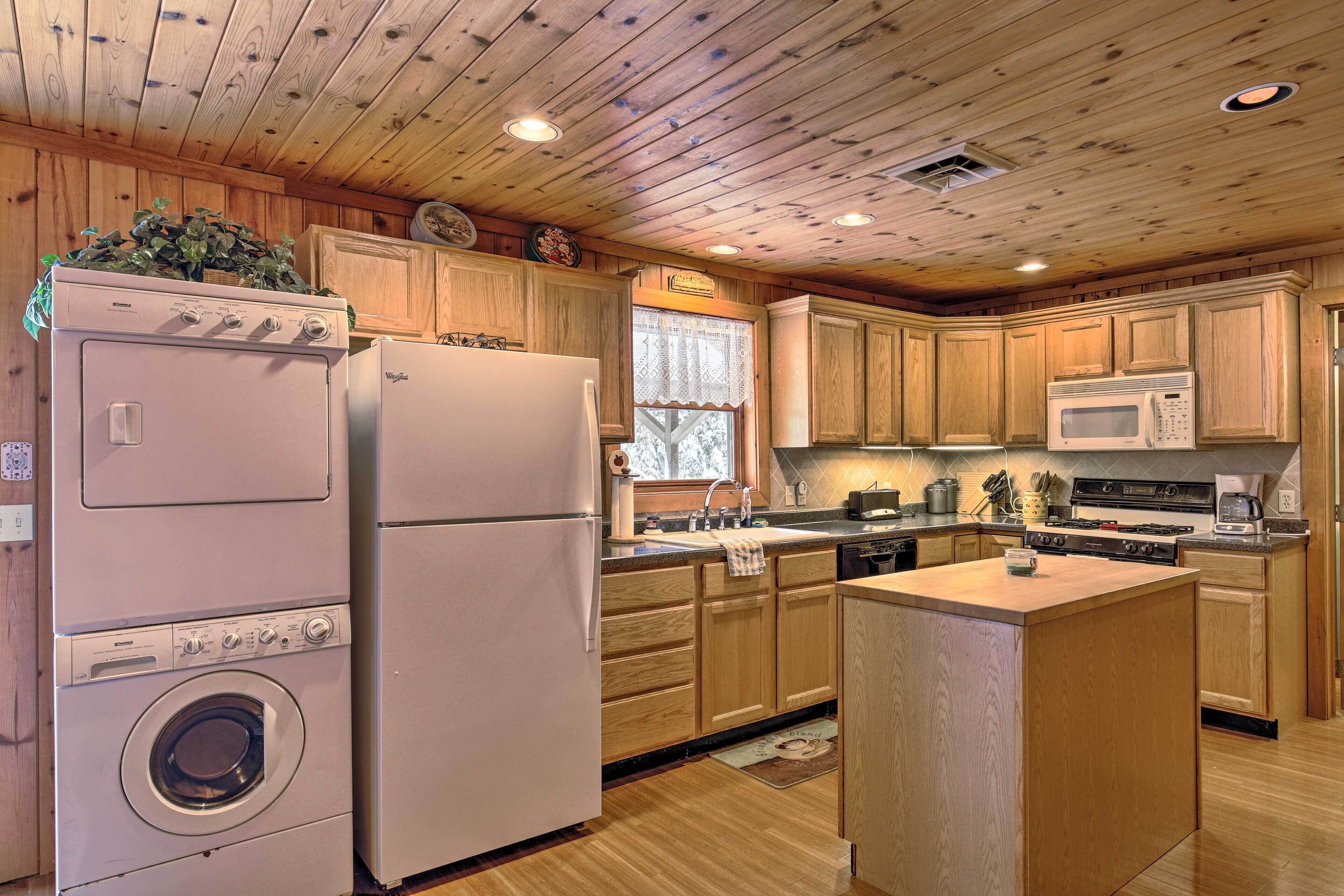 A kitchen with wooden cabinets, a washing machine, a refrigerator, a microwave, and a stove.