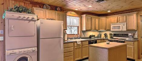 A kitchen with wooden cabinets, a washing machine, a refrigerator, a microwave, and a stove.