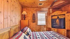 A wooden-paneled room with a bed, a television, a lamp, and a window with blinds. - Lakefront Escape w/ Fishing Pier & Snowmobiling! (Park Falls)