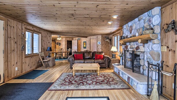 A cozy cabin interior with a stone fireplace, wooden walls, and a comfortable seating area. - Lakefront Escape w/ Fishing Pier & Snowmobiling! (Park Falls)