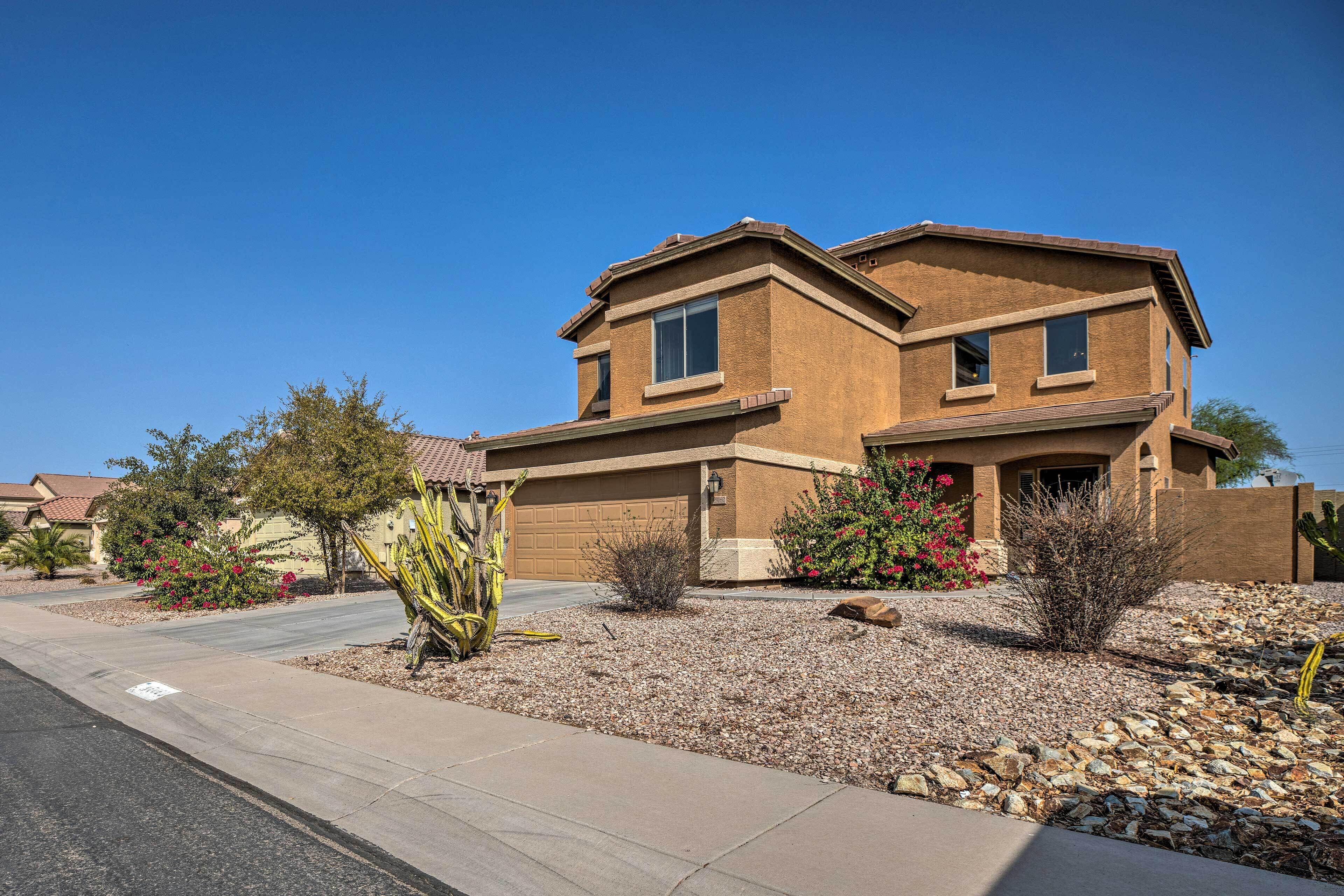 A two-story house with a garage, surrounded by a landscaped garden with cacti and flowering plants.