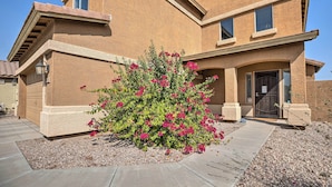 A two-story house with a stucco exterior, a front entrance with a door, and a small garden with pink flowers. - Maricopa Home w/ Outdoor Seating, 2 Mi to Golf! (Maricopa)