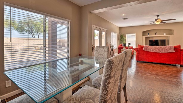 A spacious living room with a glass-top dining table, comfortable seating, a red sofa, and a ceiling fan. - Maricopa Home w/ Outdoor Seating, 2 Mi to Golf! (Maricopa)