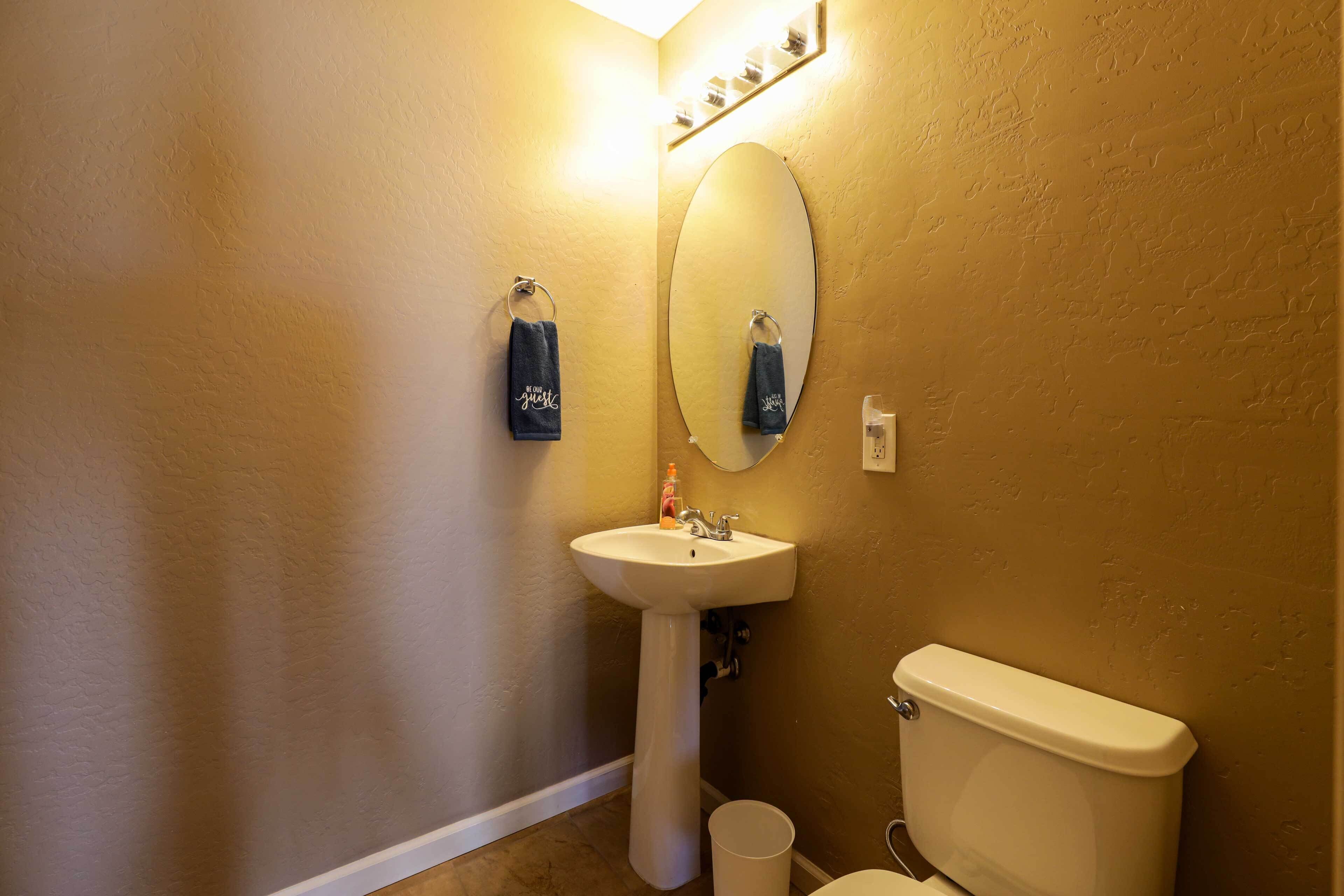 A bathroom with a pedestal sink, a toilet, and a mirror.