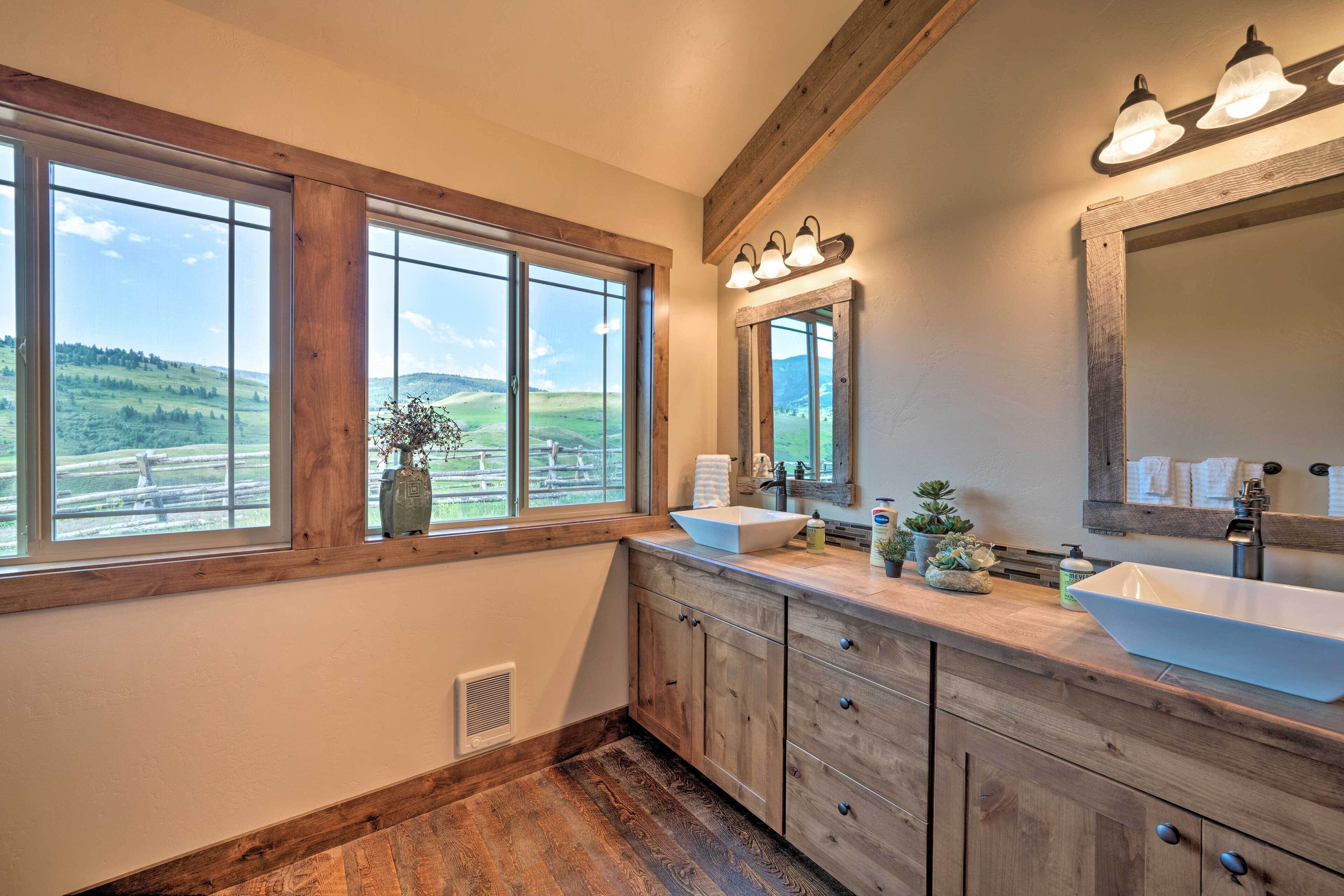 A bathroom with wooden cabinets, a large window with a view of a green landscape, and a vessel sink.