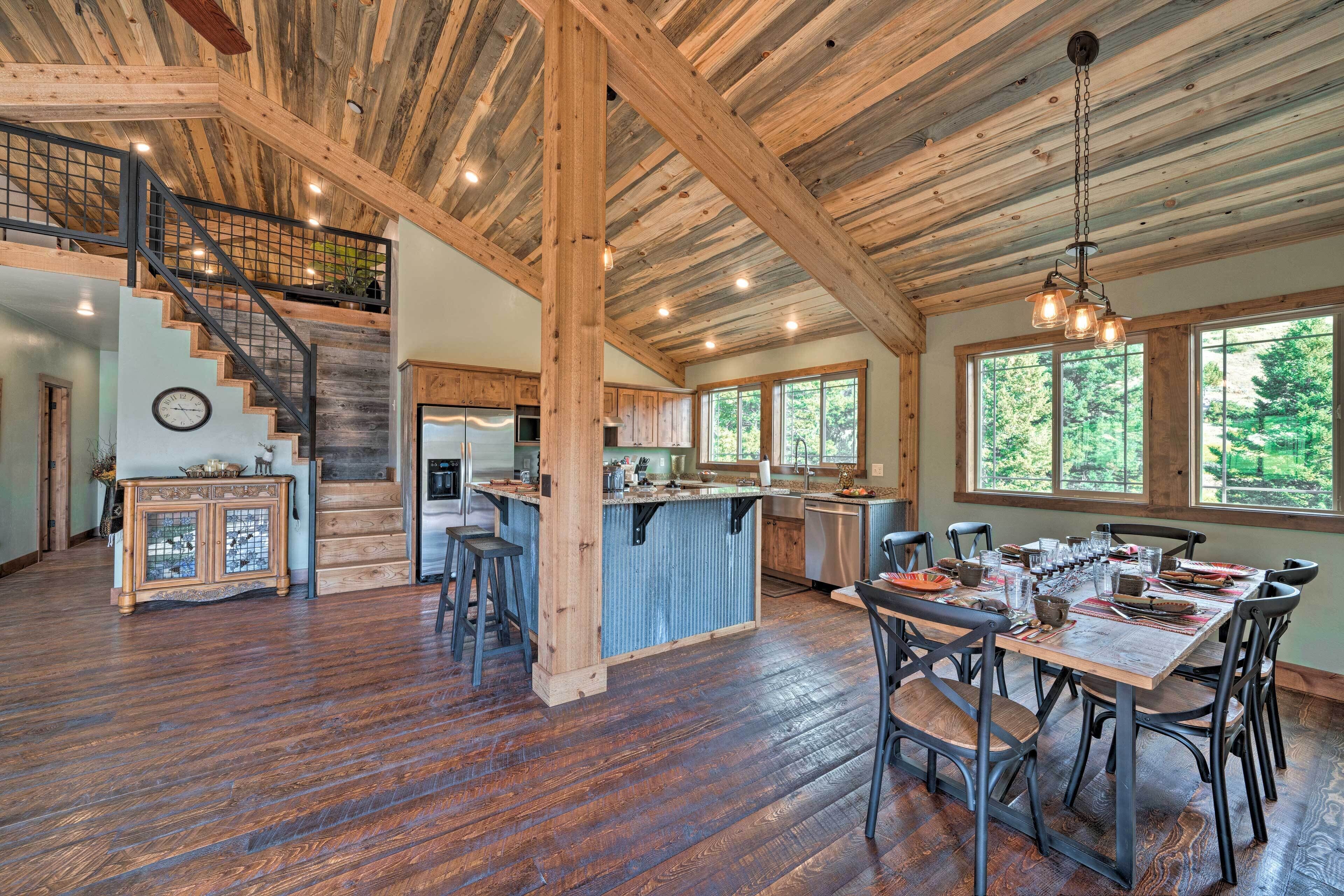A spacious kitchen with a central island, wooden beams on the ceiling, and large windows offering a view of the outdoors.