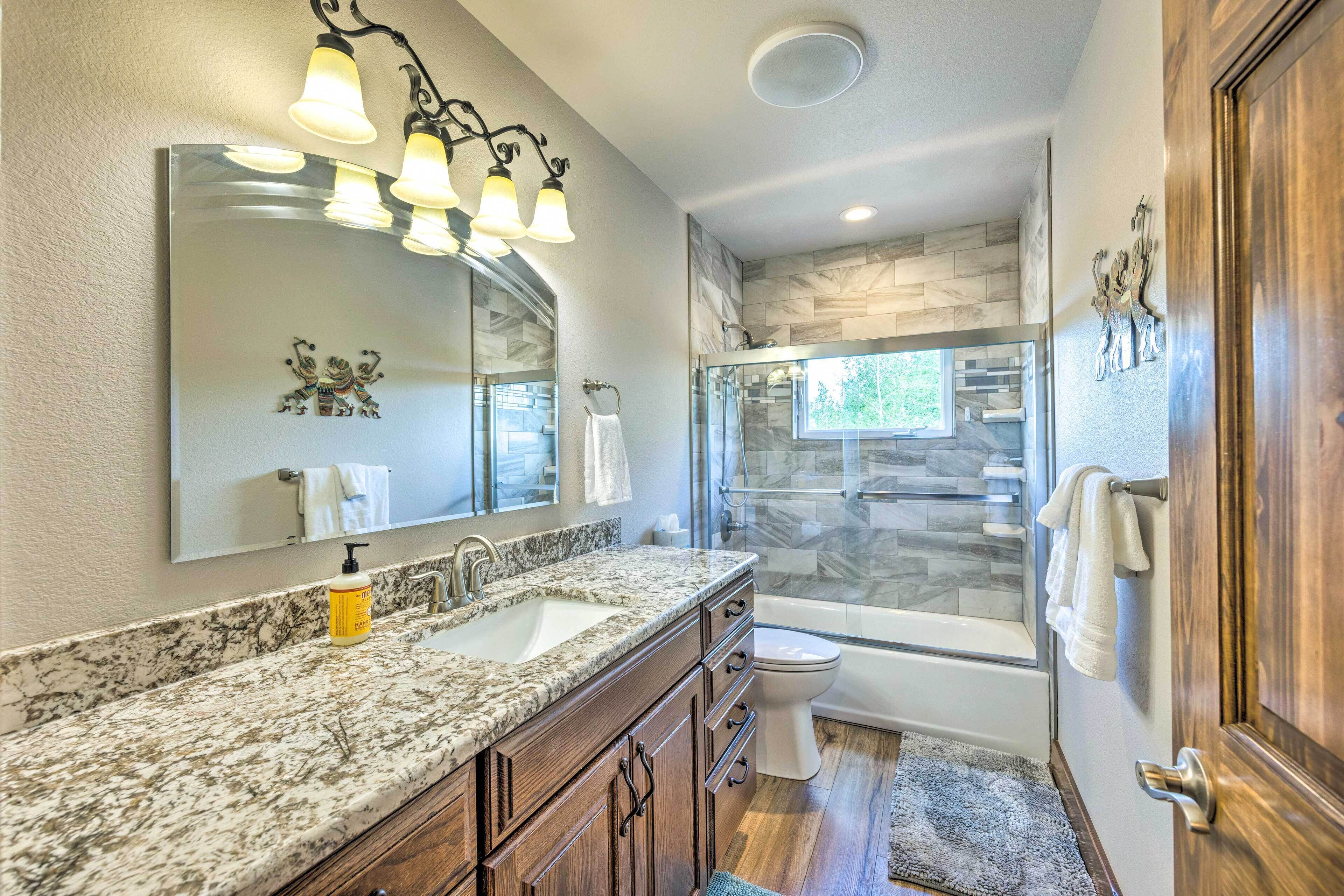 A bathroom with a granite countertop sink, a large mirror, a shower with a glass door, and a wooden door.