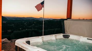 Uma banheira de hidromassagem com uma bandeira americana, rodeada por um deck de madeira e com vista para uma paisagem montanhosa.