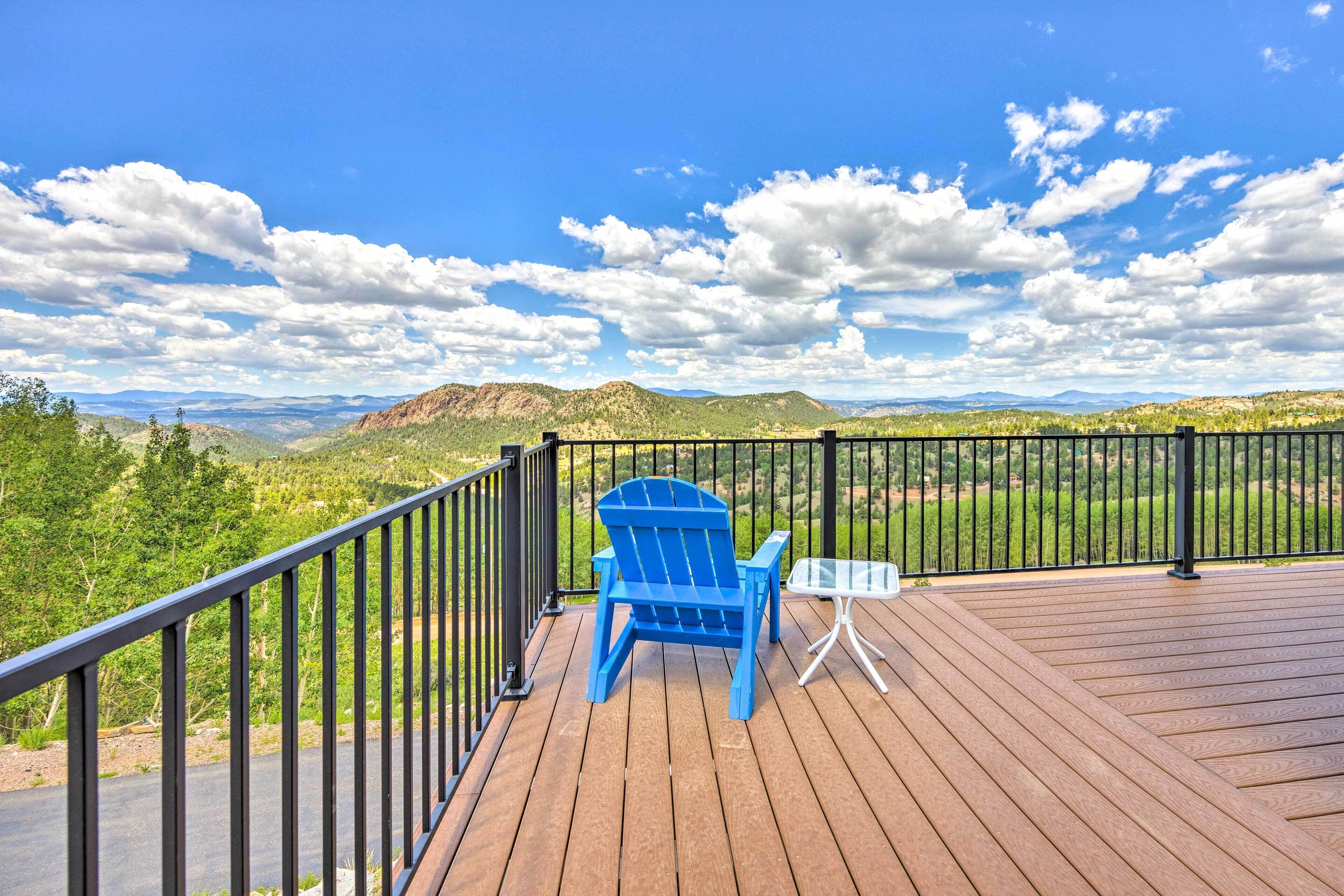 A wooden deck with a blue Adirondack chair and a small table, overlooking a mountainous landscape.