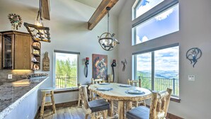 A spacious dining area with a large wooden table and chairs, surrounded by large windows offering a view of the outdoors. - Hot Tub & Mtn View! Cripple Creek Retreat (Cripple Creek)