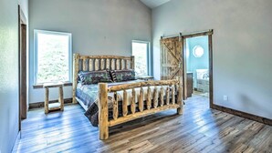 A bedroom with a wooden bed, a standing lamp, and a large window. - Hot Tub & Mtn View! Cripple Creek Retreat (Cripple Creek)