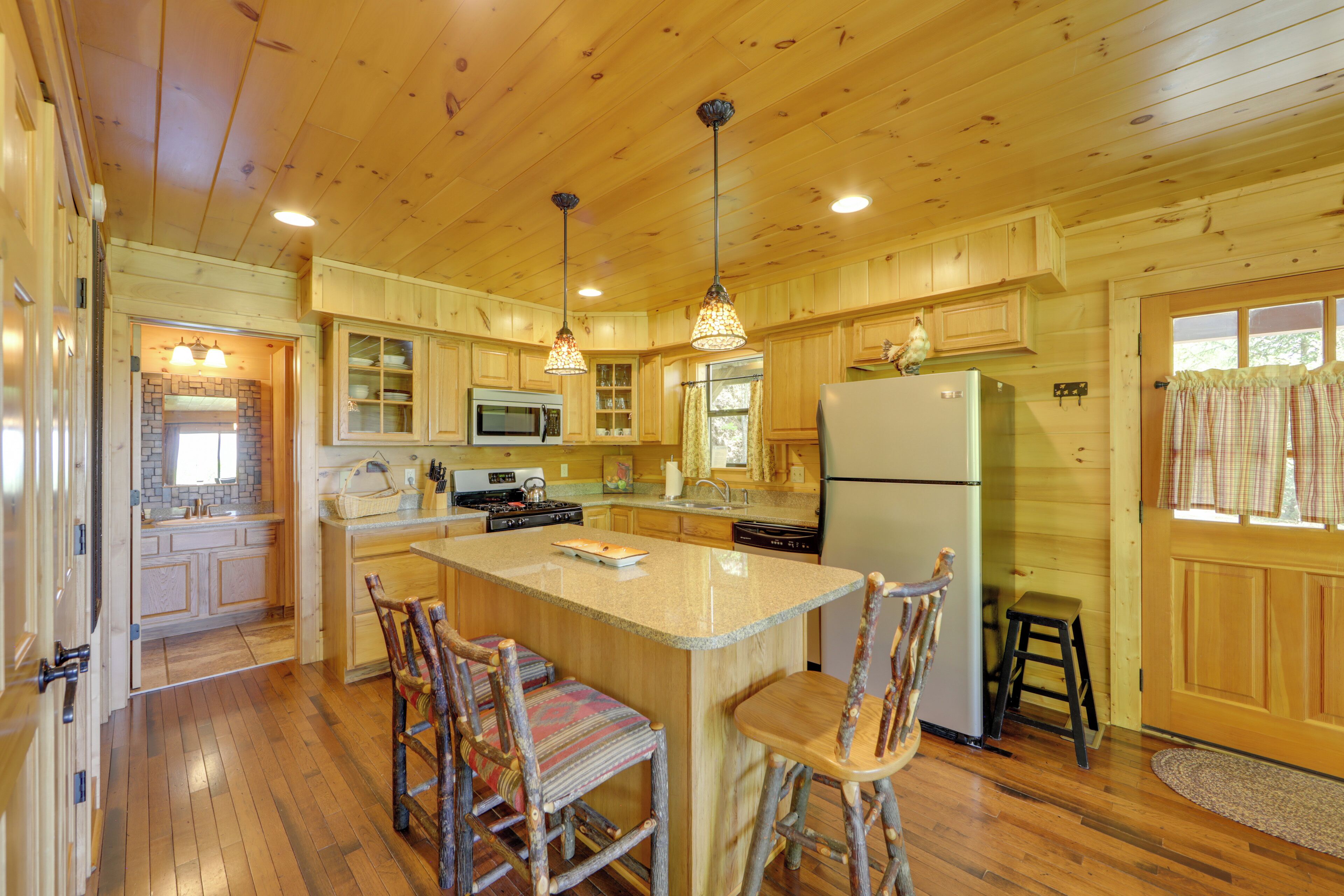 A wooden cabin kitchen with a central island, wooden chairs, a refrigerator, a microwave, and a sink.