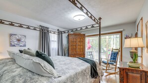Ein Schlafzimmer mit einem großen Bett, einem Holzschrank, einem Schaukelstuhl und Blick ins Freie.