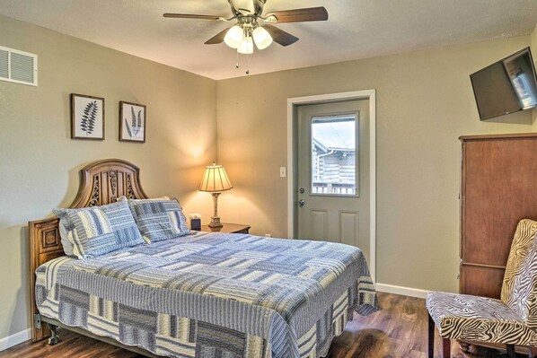 A bedroom with a bed, a ceiling fan, a lamp, a door, and a television mounted on the wall.