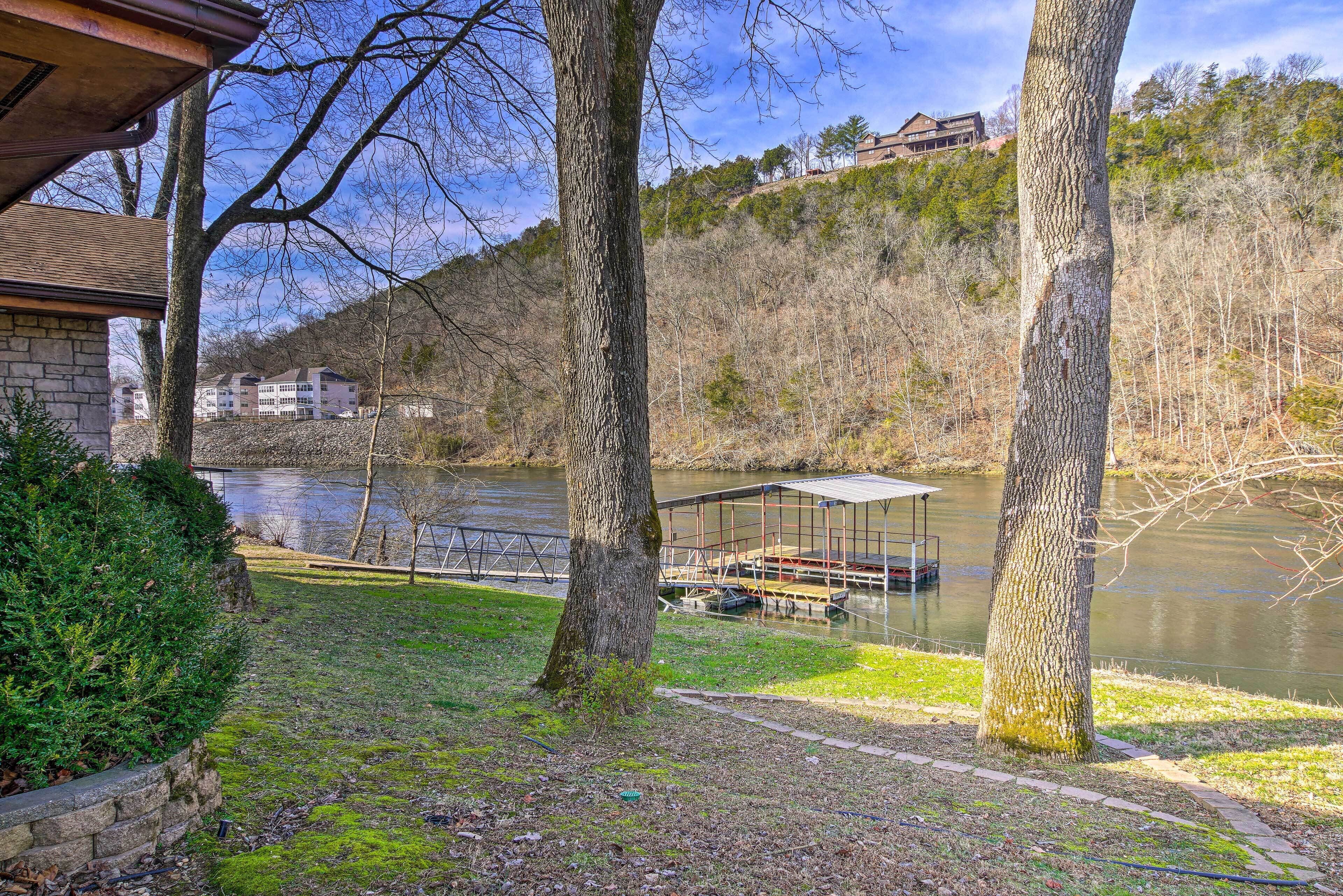 A lakeside property with a dock, a covered boat house, and a stone building in the background.