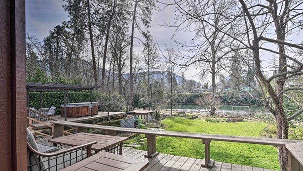 A wooden deck with outdoor seating, a barbecue area, and a view of a lake and mountains. - Hot Tub & Views: Spacious Getaway on Rogue River (Grants Pass)