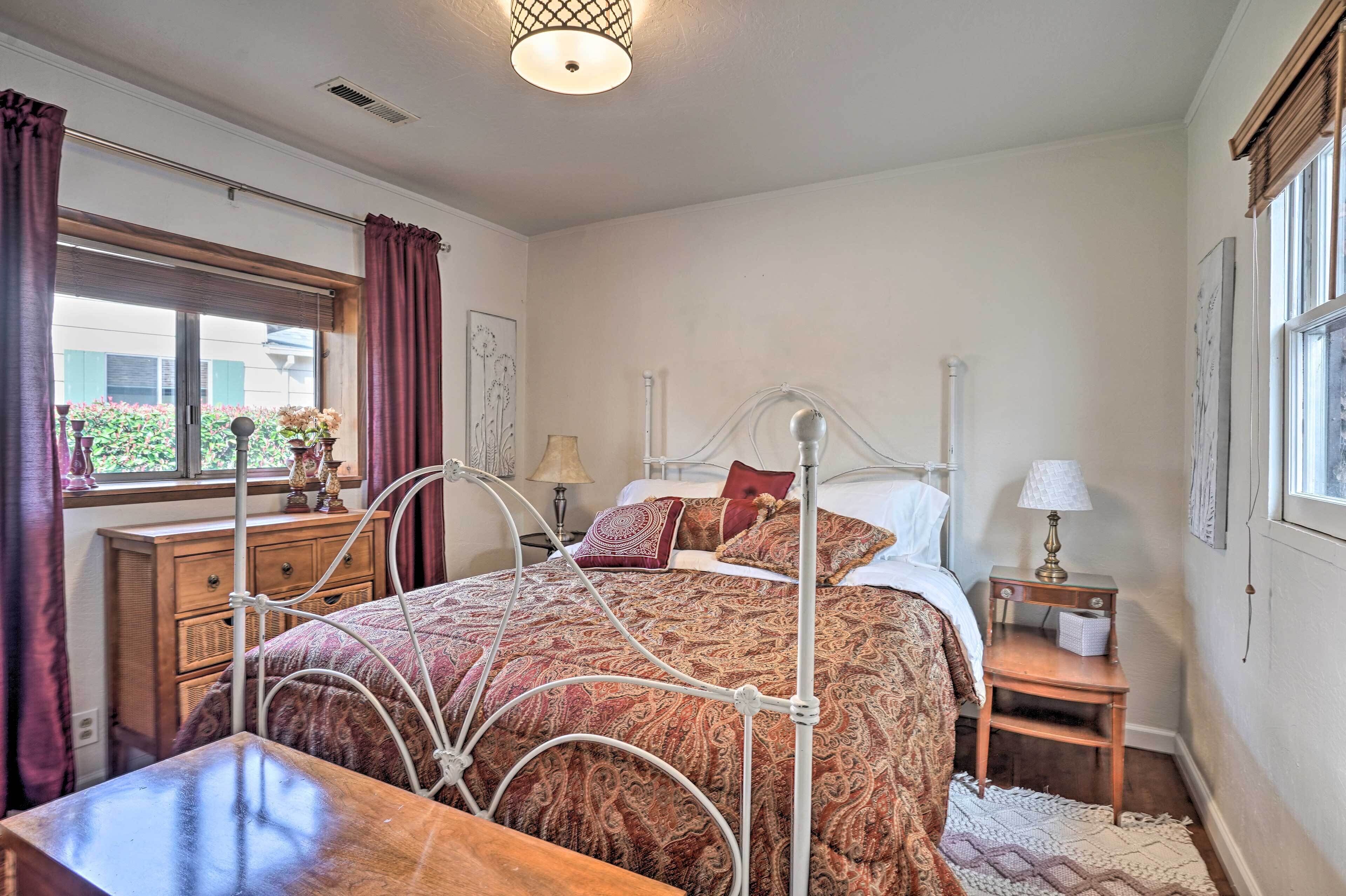 A neatly arranged bedroom with a metal bed frame, a bedside table with a lamp, and a window with curtains.