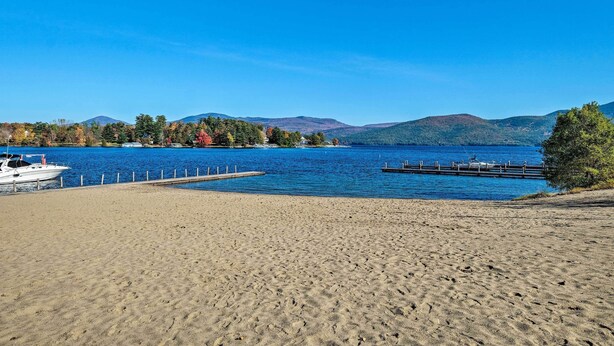 A beach with a dock and a boat, surrounded by mountains and trees. - Walk to Beach! Bolton Landing Cottage w/ Deck (Bolton Landing)