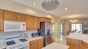 A modern kitchen with wooden cabinets, a stainless steel refrigerator, a microwave, a stove, and a chandelier. - 3 Mi to Lake Havasu: Luxe Home w/ Pool & Spa! (Lake Havasu City)