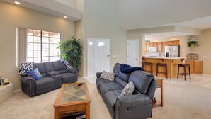 A spacious living room with a large sofa, a coffee table, and a kitchen area with wooden cabinets and a bar stool. - 3 Mi to Lake Havasu: Luxe Home w/ Pool & Spa! (Lake Havasu City)