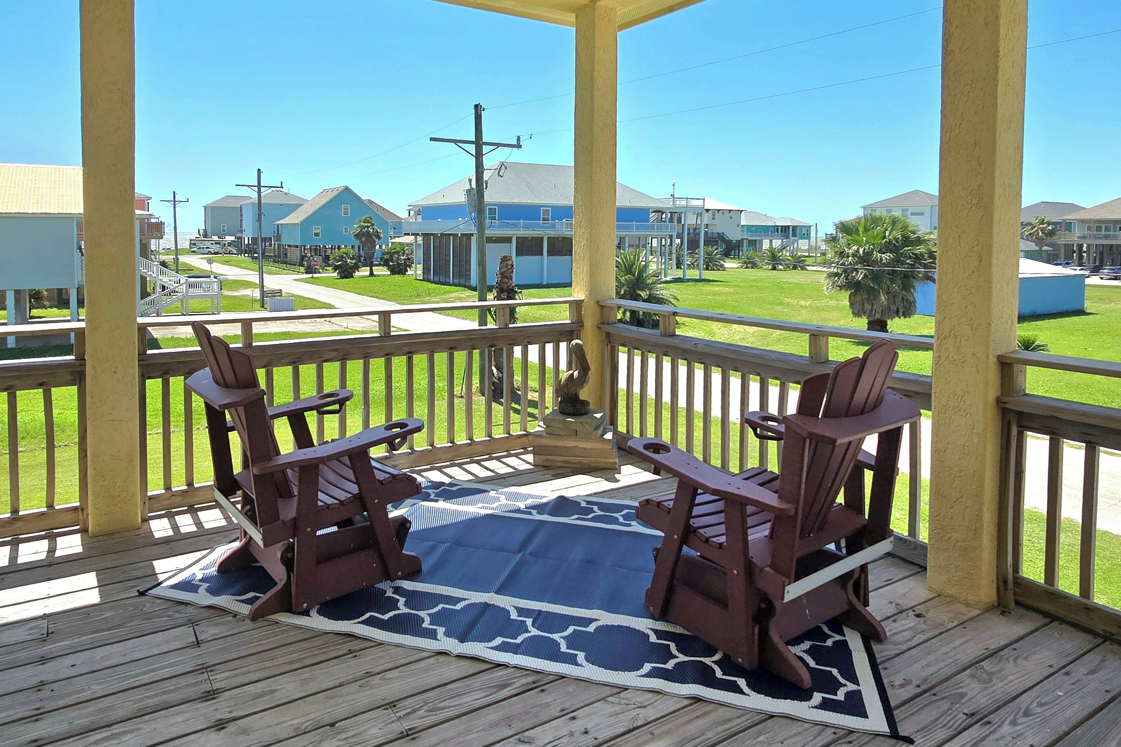 A covered porch with two Adirondack chairs and a blue patterned rug.