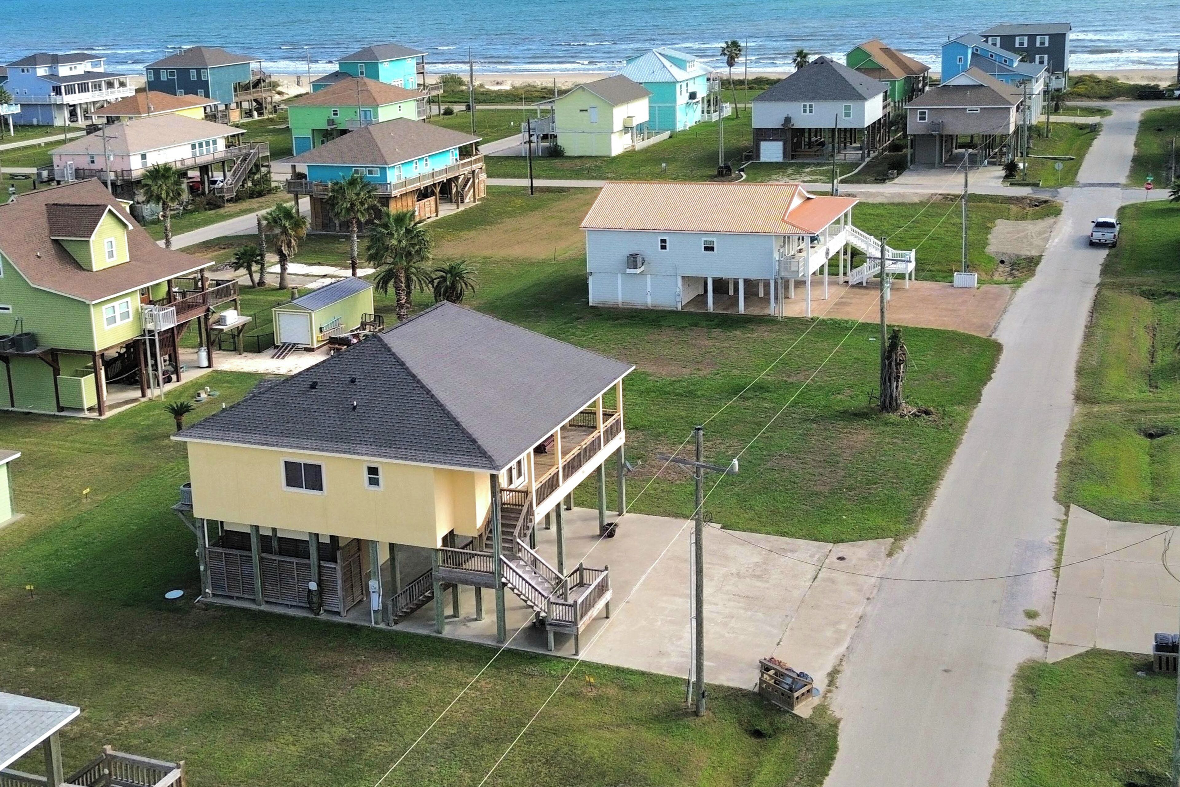A coastal residential area with houses, a road, and a beach in the background.