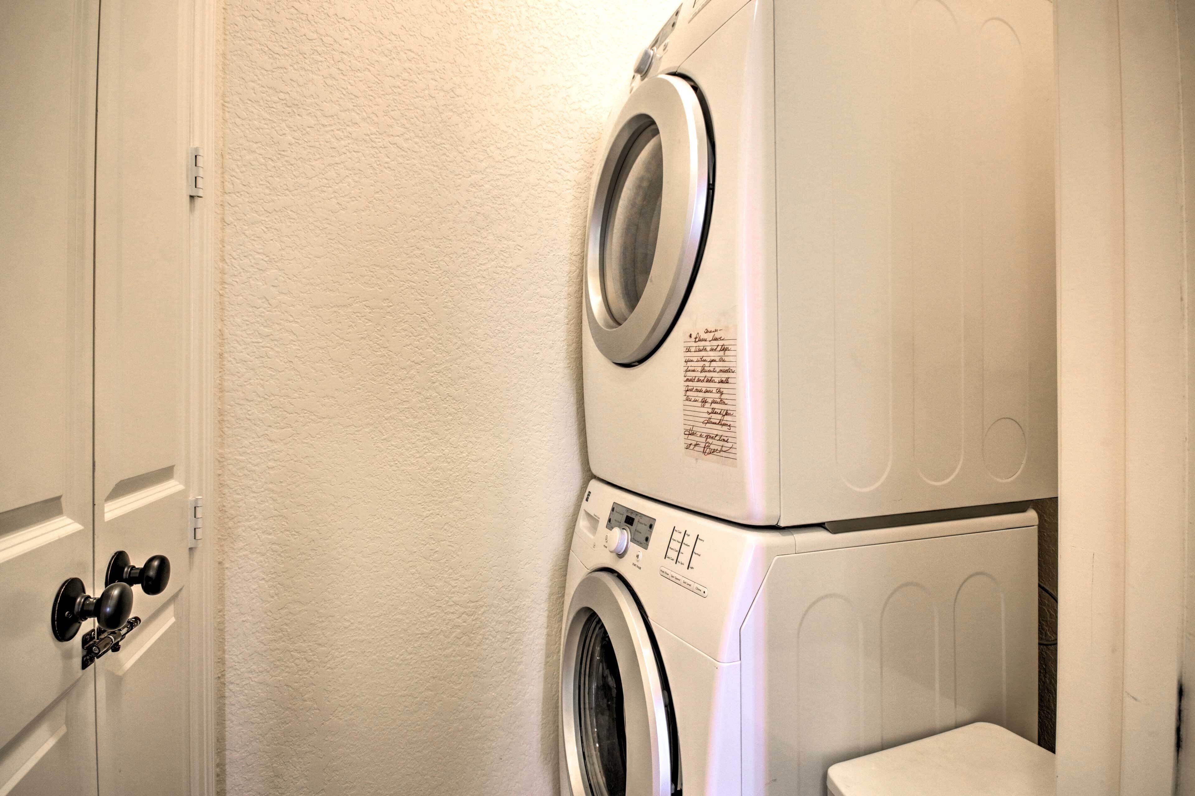 Une machine à laver et un sèche-linge superposés dans une buanderie, avec une porte blanche et un mur à texture.