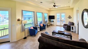 A spacious living room with a balcony, large windows, a ceiling fan, and a television. - Dog-friendly Casa Sol House in Crystal Beach! (Port Bolivar)