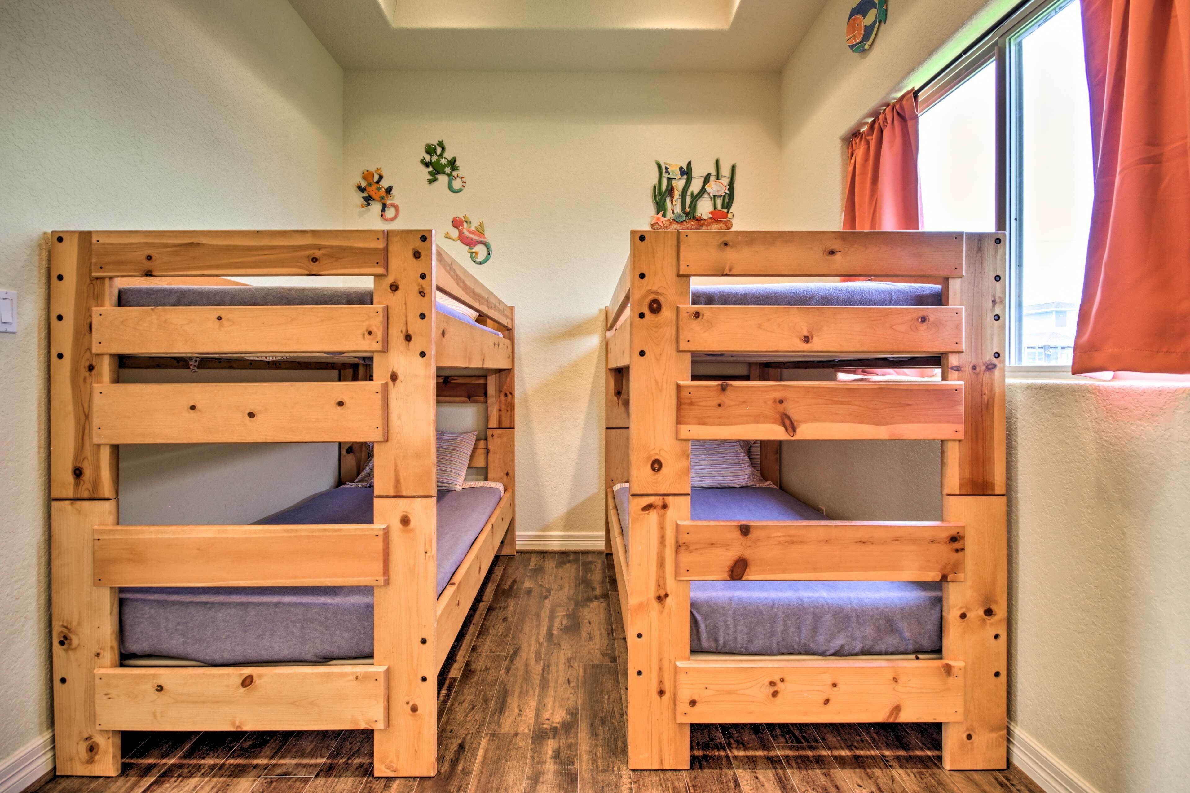 Two bunk beds with wooden frames and blue bedding, a window with orange curtains, and wall decorations including a cactus and a fish.