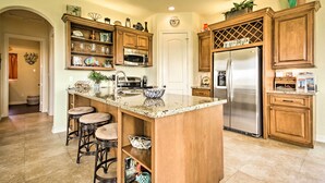 A kitchen with a central island, bar stools, wooden cabinets, stainless steel appliances, and a decorative sign. - Dog-friendly Casa Sol House in Crystal Beach! (Port Bolivar)