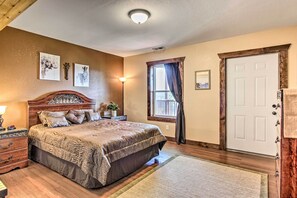A bedroom with a wooden bed, a nightstand, a lamp, a window with curtains, and a door.