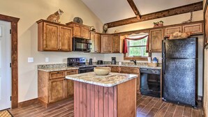 A kitchen with wooden cabinets, a granite countertop, a black refrigerator, and a built-in island with a bowl.