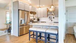 A modern kitchen with stainless steel appliances, white cabinetry, and a central island with bar stools. - Waterfront Maryland Vacation Home: Private Beach! (Ridge)