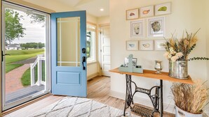 A room with a blue door, a wooden table, and a metal chair. There are framed pictures on the wall and a vase with dried plants. - Waterfront Maryland Vacation Home: Private Beach! (Ridge)