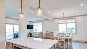 A spacious kitchen with a large island, white cabinetry, and pendant lighting. There is a dining area with a table and chairs, and a TV mounted on the wall. - Waterfront Maryland Vacation Home: Private Beach! (Ridge)