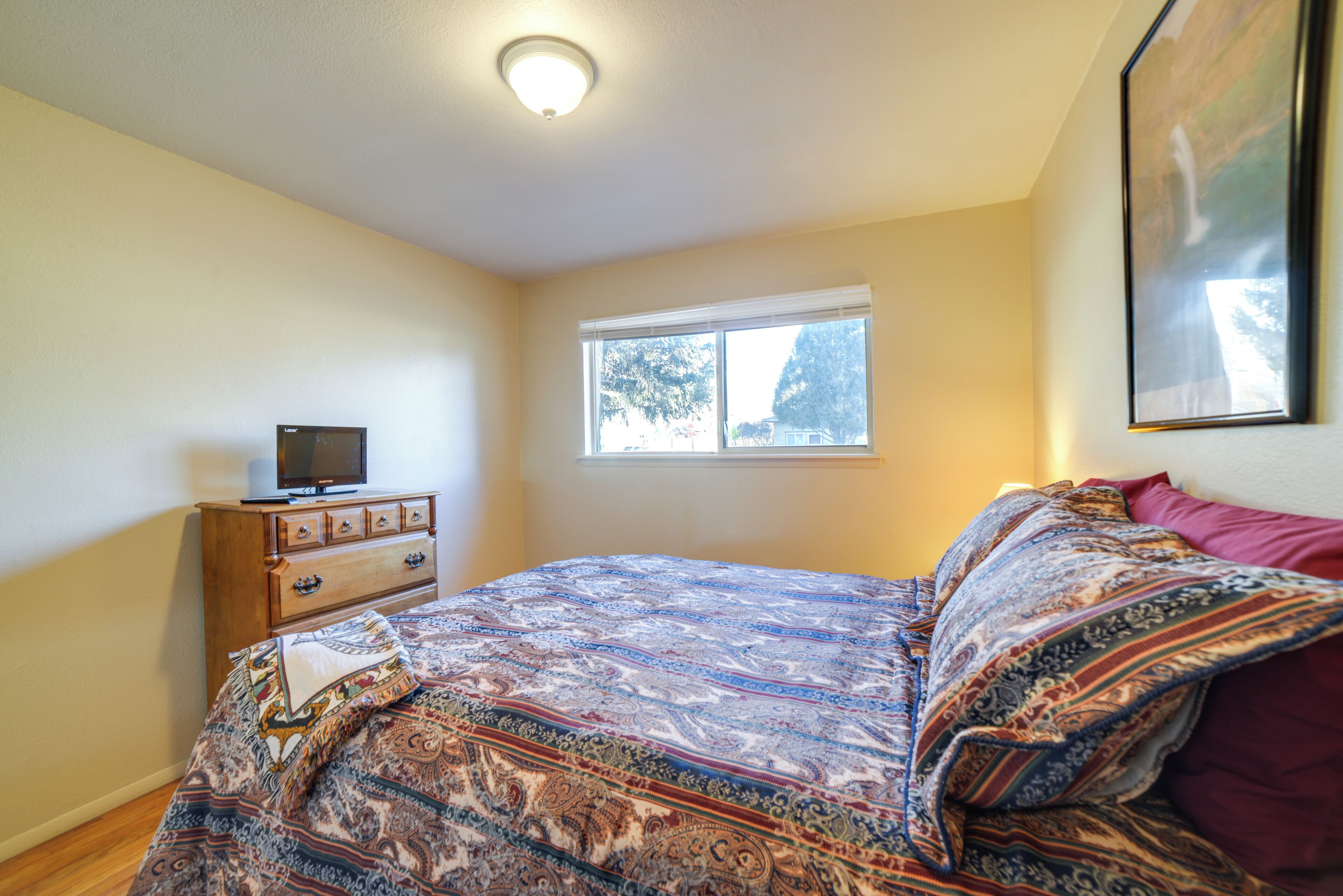 Une chambre à coucher avec un lit, une commode, un téléviseur posé sur la commode et une fenêtre.