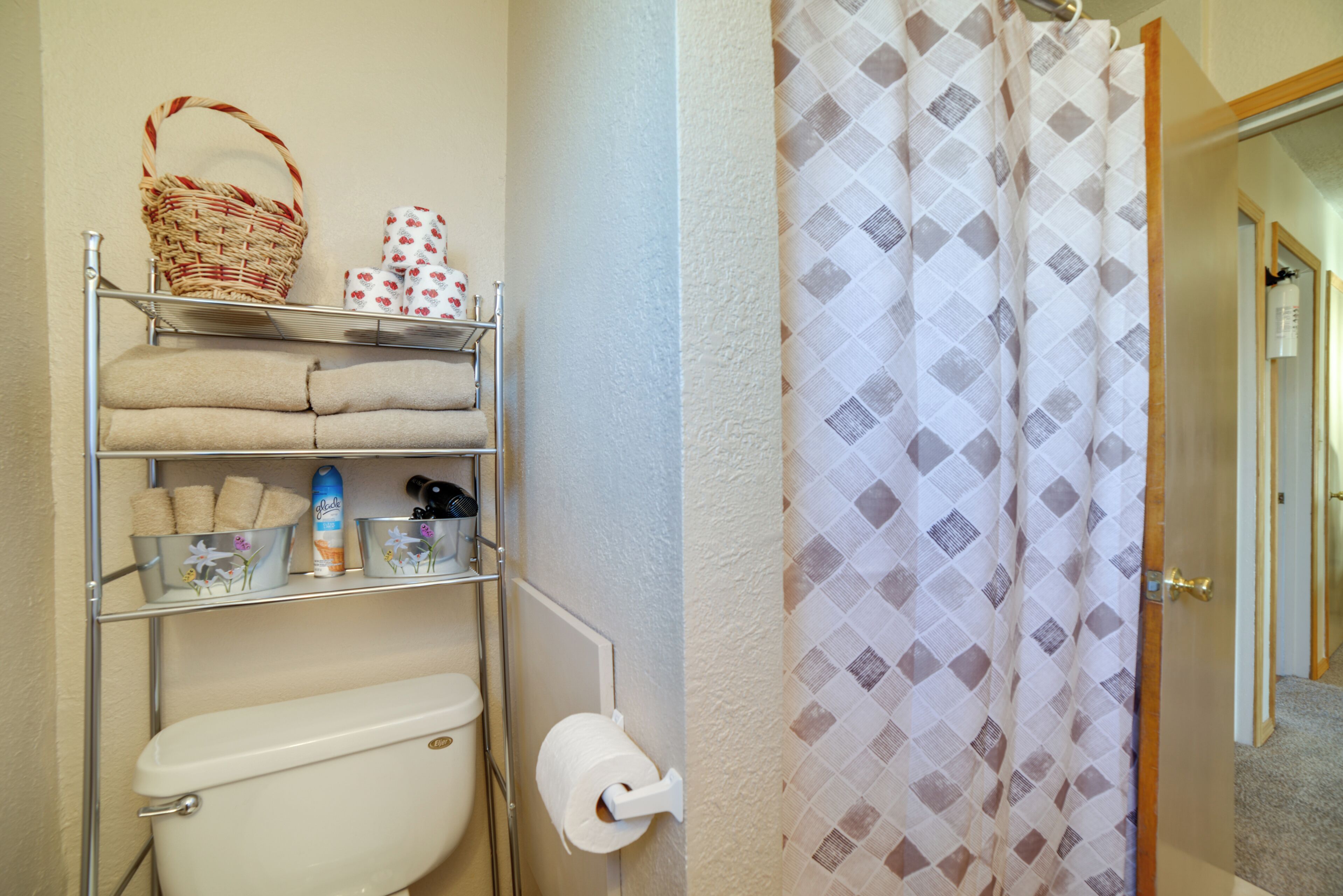 Un baño con inodoro, repisas con toallas y artículos de aseo, y cortina de ducha.