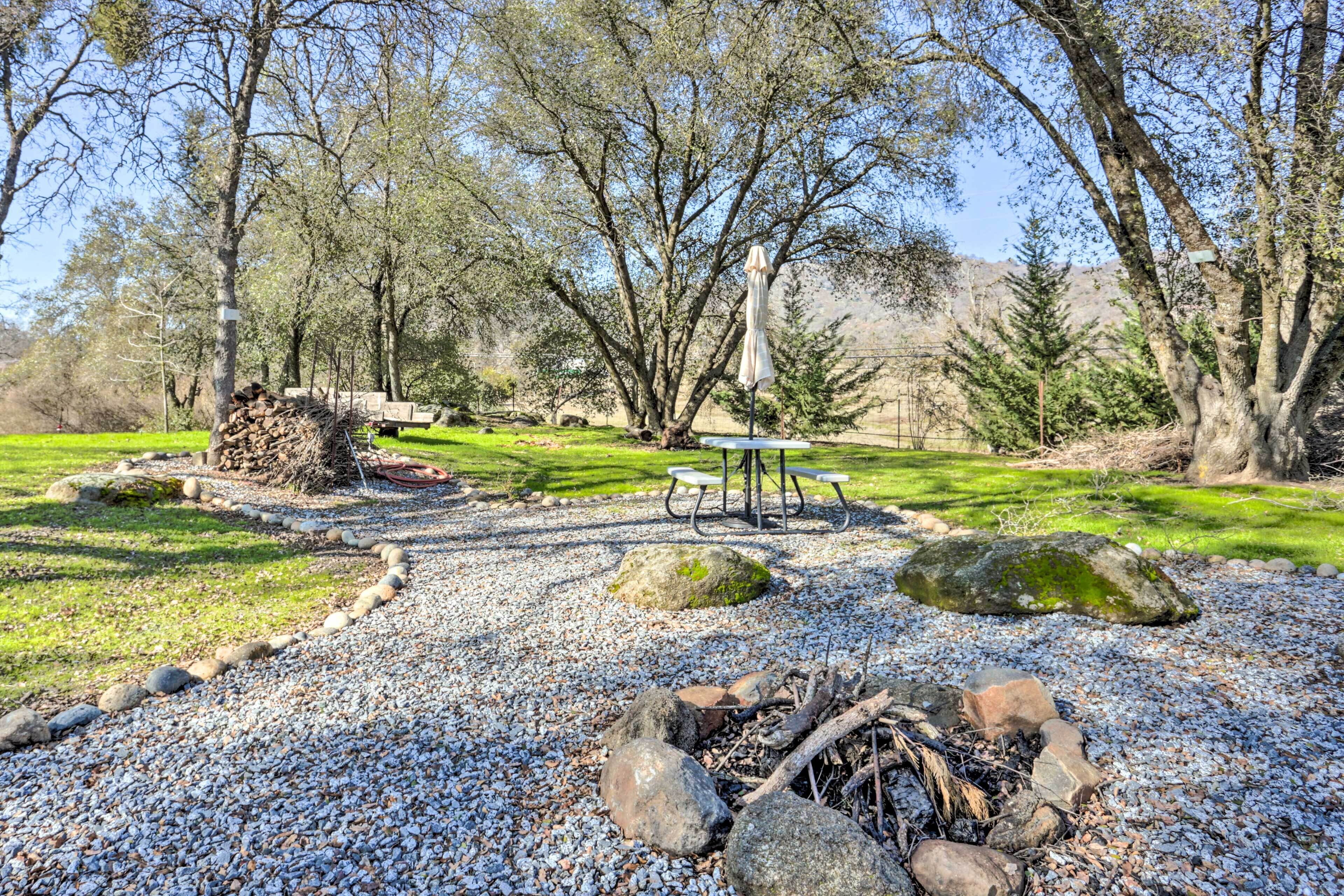 A park with a gravel path, picnic tables, a fire pit, and trees.