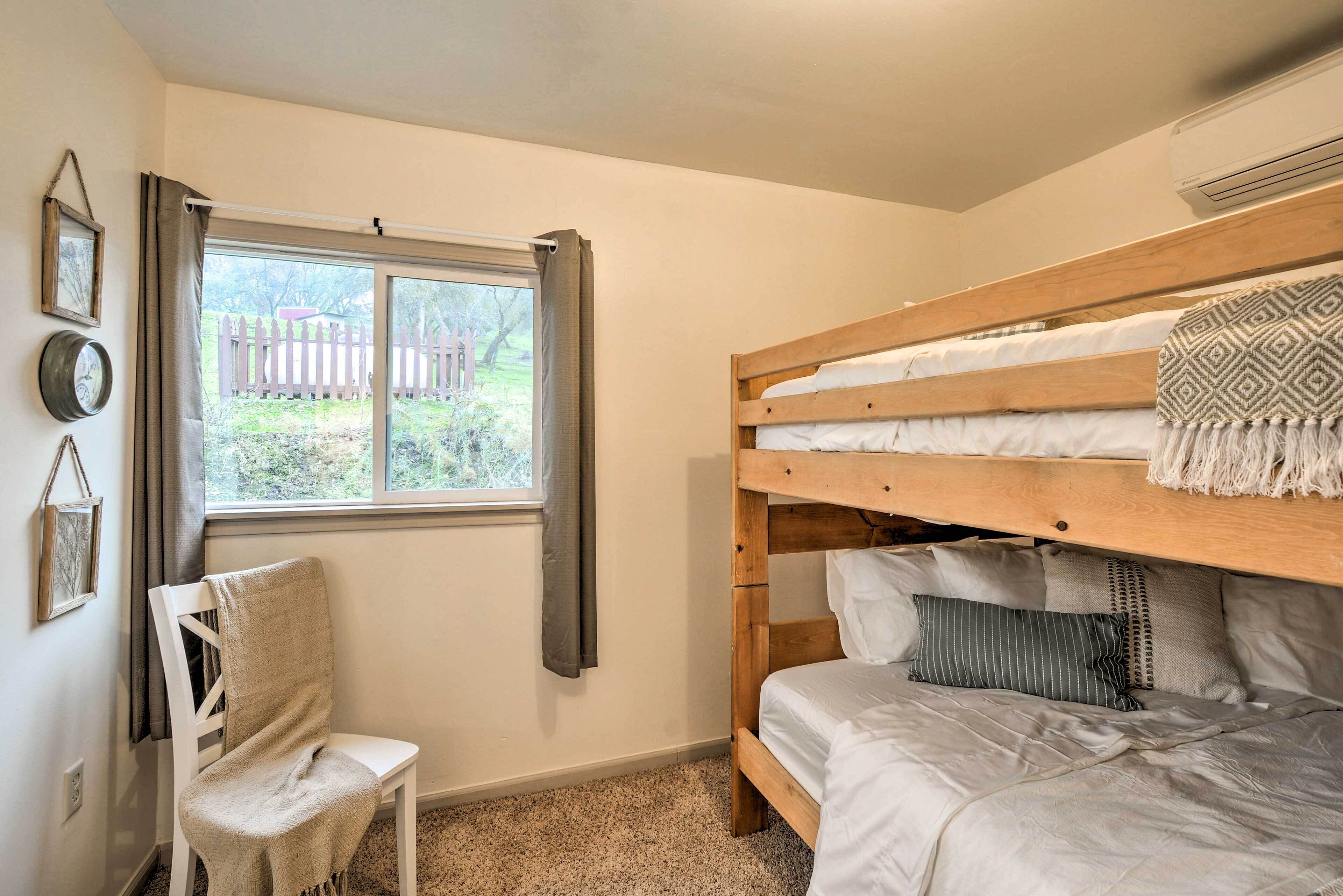 A bunk bed with a wooden frame, a chair with a blanket, a window with curtains, and a wall-mounted air conditioner.