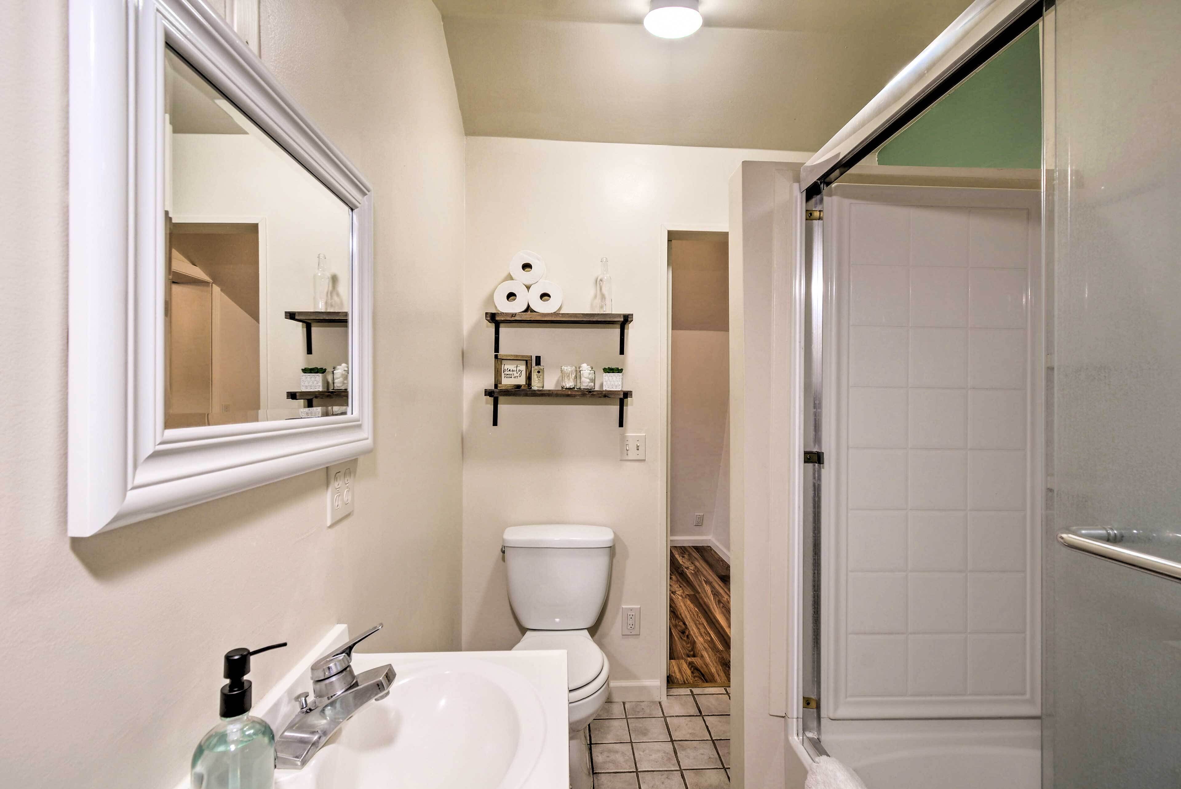 A bathroom with a white sink, a toilet, and a shower. There are shelves above the toilet with toiletries.