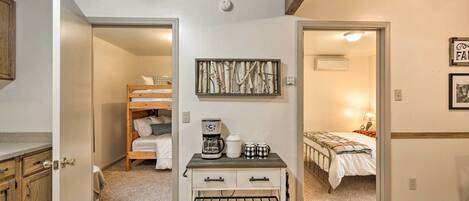 Una habitación compacta con una cama litera, una kitchenette pequeña con cafetera y un estante con un reloj.