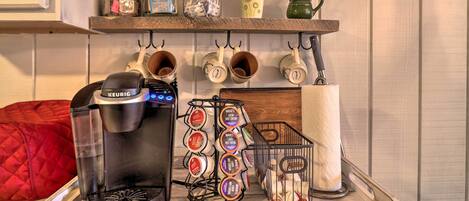 A kitchen with a Keurig coffee maker, a mug rack, and various kitchen items on shelves.