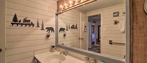 Une salle de bain avec un lavabo blanc, un lambris en bois, un miroir avec éclairage intégré et des décorations sur le thème des animaux.