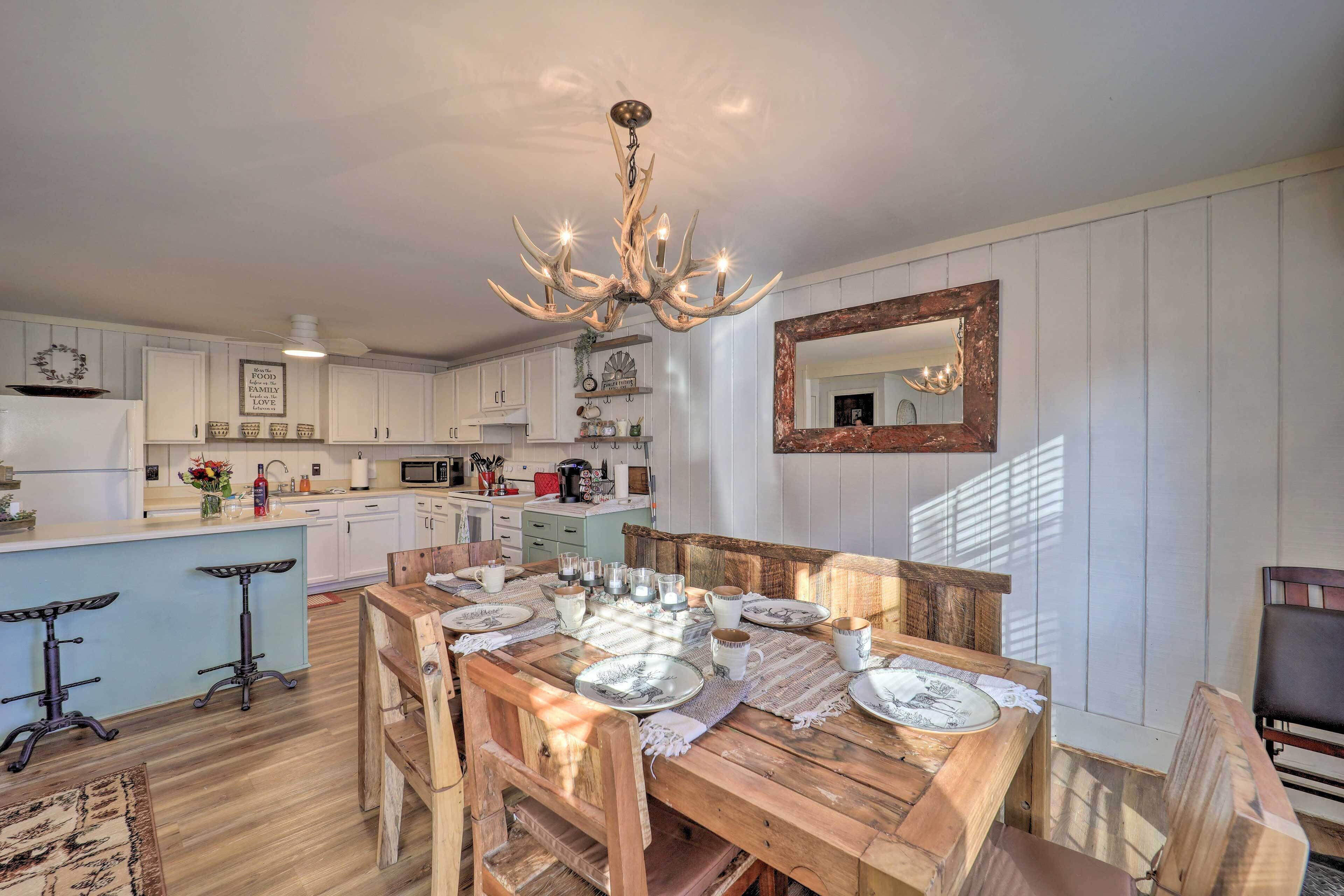 A kitchen with a wooden dining table set for six, white cabinets, a chandelier, and a rustic mirror.