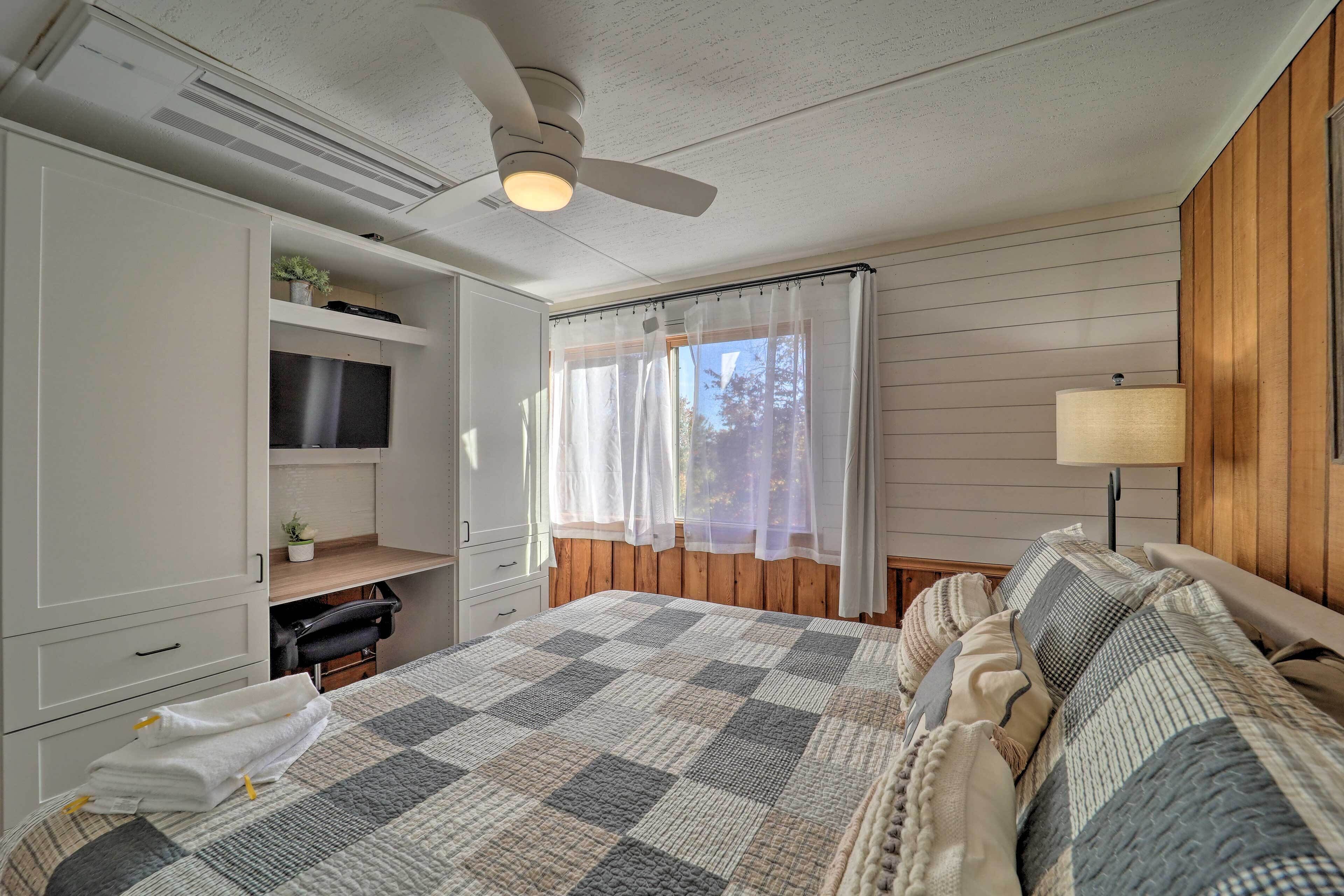 A bedroom with a large bed, a ceiling fan, a TV on a shelf, and a window with curtains.