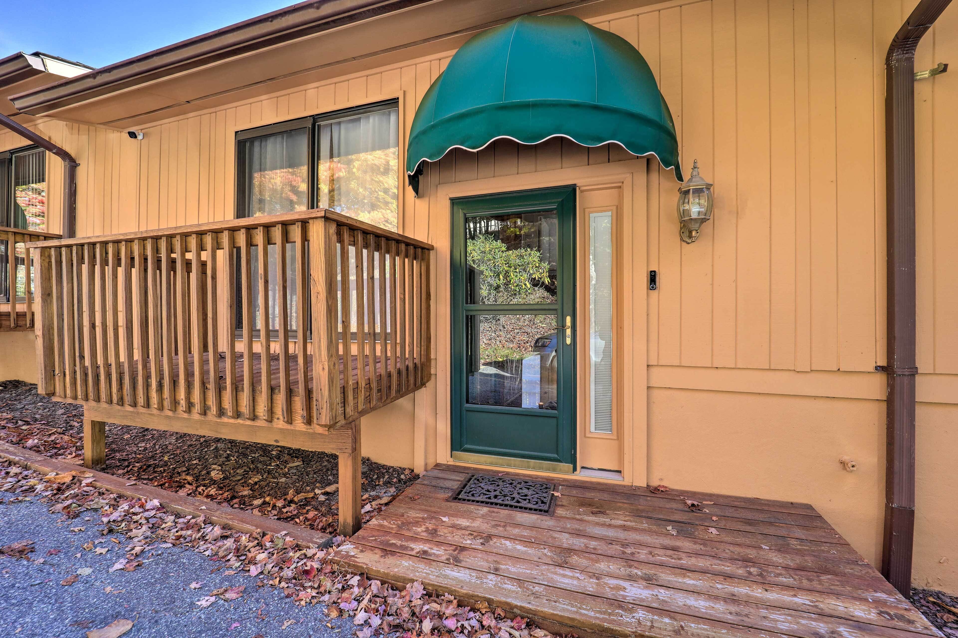 Une terrasse en bois mène à une maison avec une porte verte et un auvent vert.